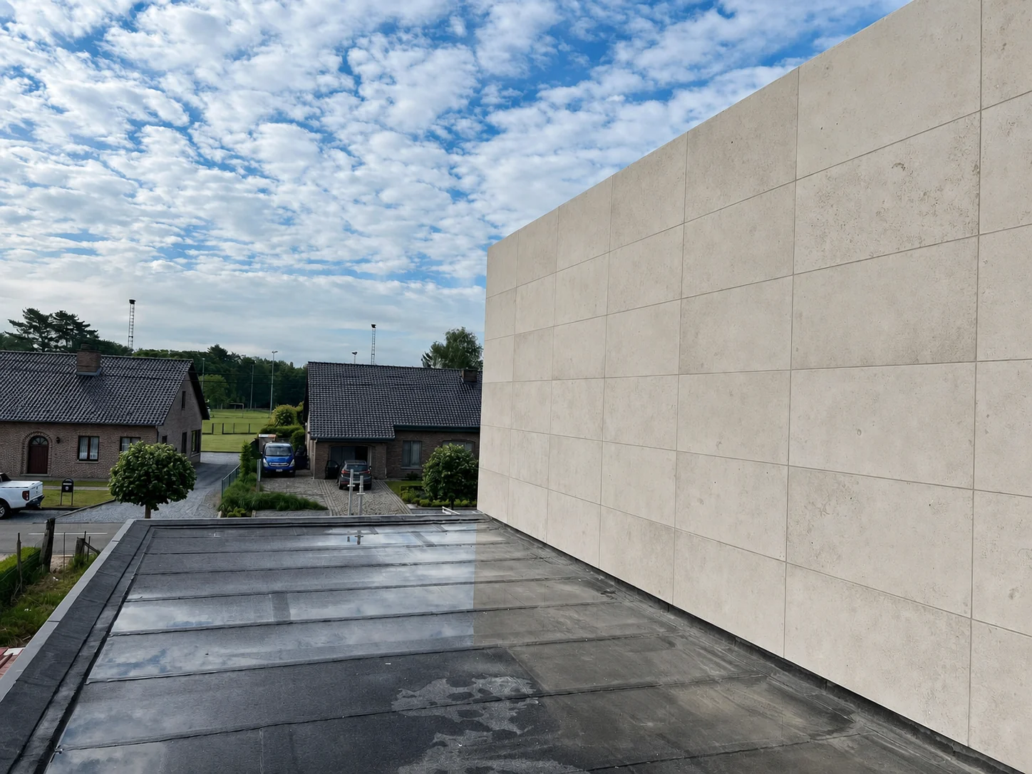 Long mur de façade clair à joints réguliers sous un ciel bleu à Genk